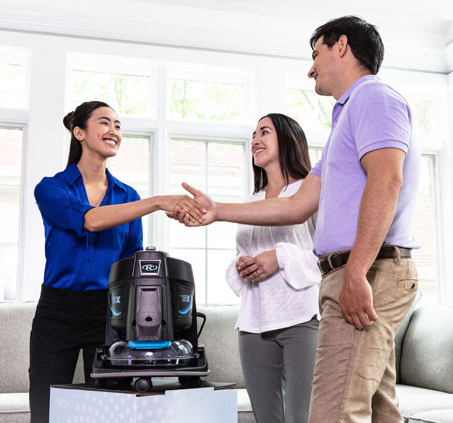 Two women and a man shaking hands with a Rainbow SRX on demo display box
