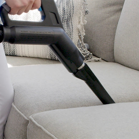 Person cleaning a gray sofa with a Rainbow vacuum with crevice tool attachment.