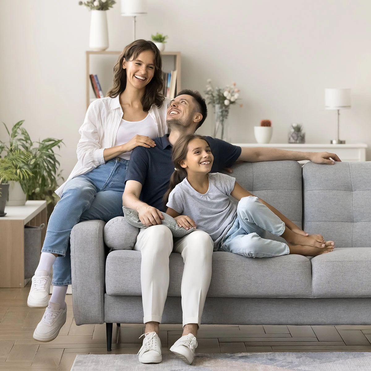 Family of three sitting on a gray couch in a living room.